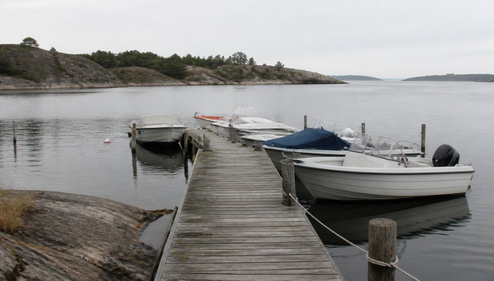 Träbrygga med förtöjda småbåtar i en lugn svensk skärgårdsvik